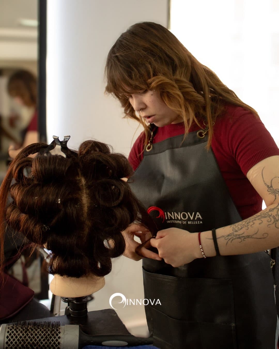 Alumna con delantal de Instituto Innova armando un peinado en una cabeza de práctica